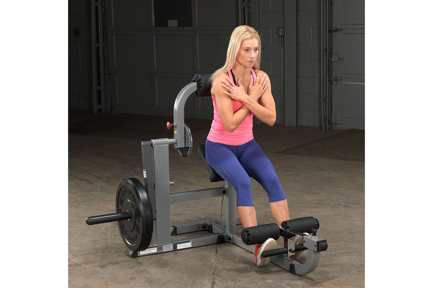 Woman wearing hot pink sleeveless tank and navy capri leggings using gray and black ab and back exercise machine in gym setti