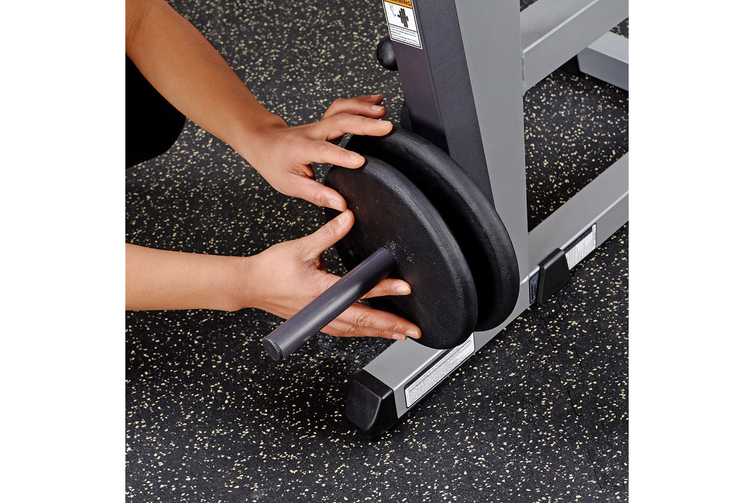 Hand gripping black padded handle of Body-Solid Ab & Back Machine on speckled gym floor