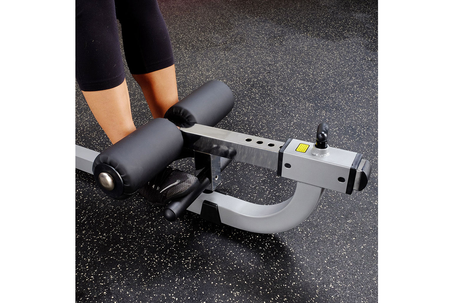 Person in black leggings using gray and black ab and back exercise machine on speckled gym floor
