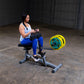 Woman using commercial seated calf raise machine with yellow weight plates in industrial gym setting
