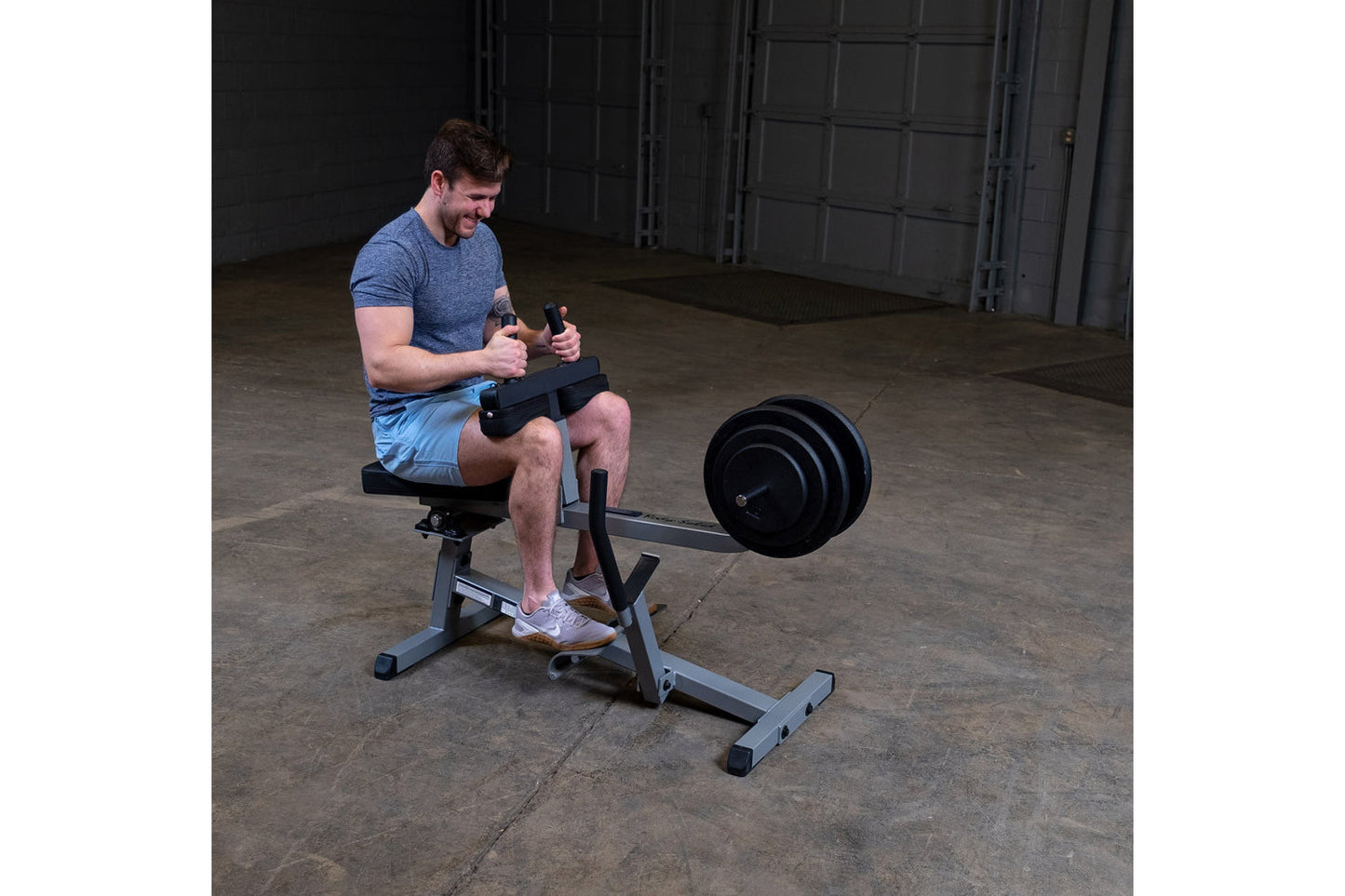 Man in blue t-shirt and light blue shorts using black and gray seated calf raise machine with weight plates in gym