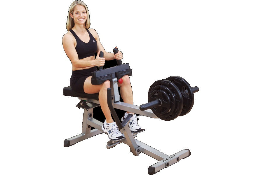 Woman using Body-Solid commercial seated calf raise machine with black weight plates, gray frame, and padded seat on white ba