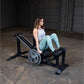 Woman using black leg press machine with loaded barbell in industrial gym setting
