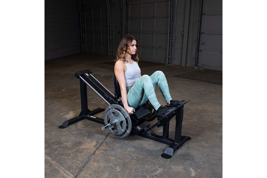 Woman using black leg press machine with loaded barbell in industrial gym setting