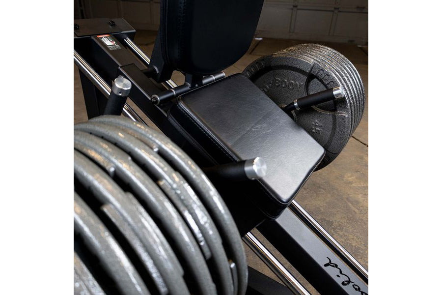 Body-Solid leg press machine with black metal frame, padded seat, and loaded weight plates in home gym setting