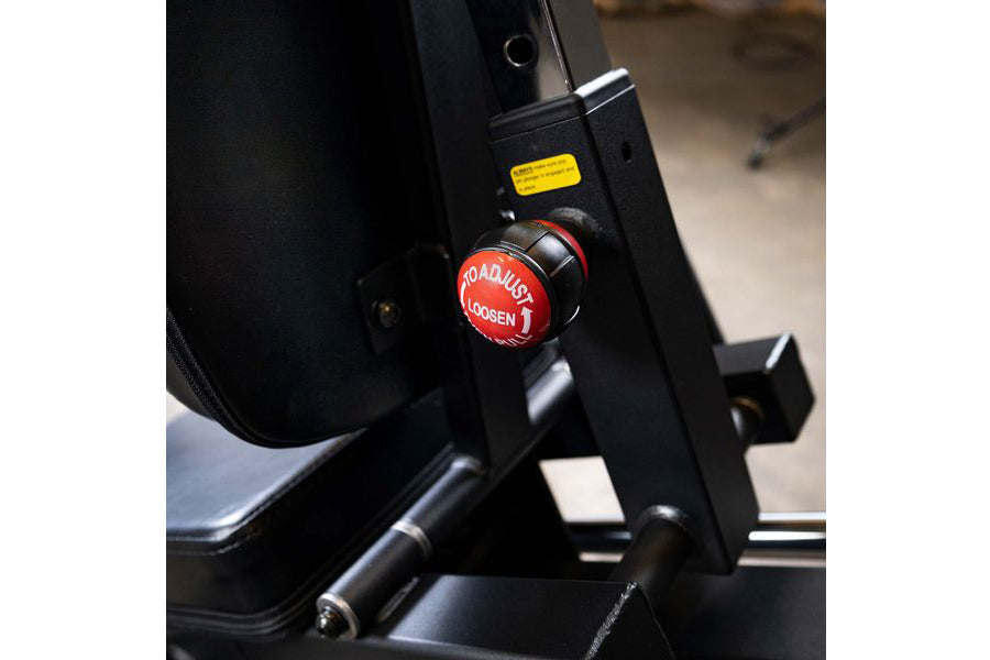 Black leg press machine with red "Roadbusy" brand knob and yellow warning label, close-up detail view