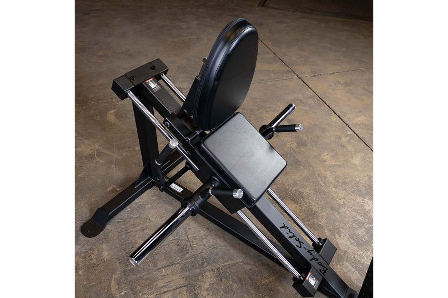 Black compact leg press machine with gray padded seat and backrest, chrome foot plate, on concrete floor