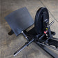 Black compact leg press machine with textured foot platform and weight plate loaded on concrete floor