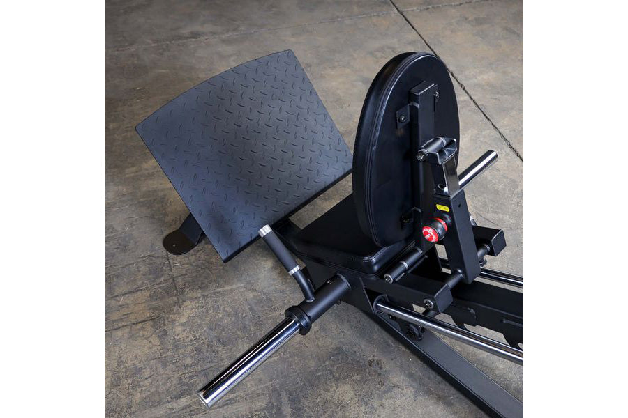 Black compact leg press machine with textured foot platform and weight plate loaded on concrete floor