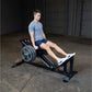 Man wearing light blue t-shirt and dark shorts using black Body-Solid leg press machine in gym setting