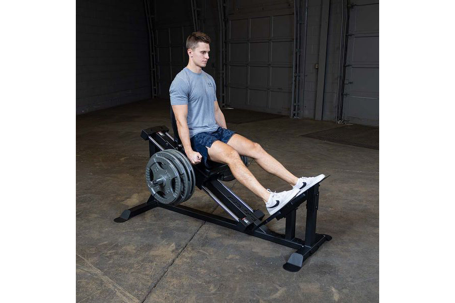 Man wearing light blue t-shirt and dark shorts using black Body-Solid leg press machine in gym setting