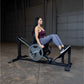 Woman using black leg press machine with weighted plate loaded, in garage gym setting