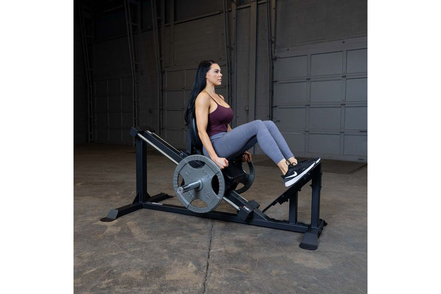 Woman using black leg press machine with weighted plate loaded, in garage gym setting