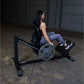 Woman using black leg press machine with weighted plate, wearing purple leggings and black sneakers in gym setting