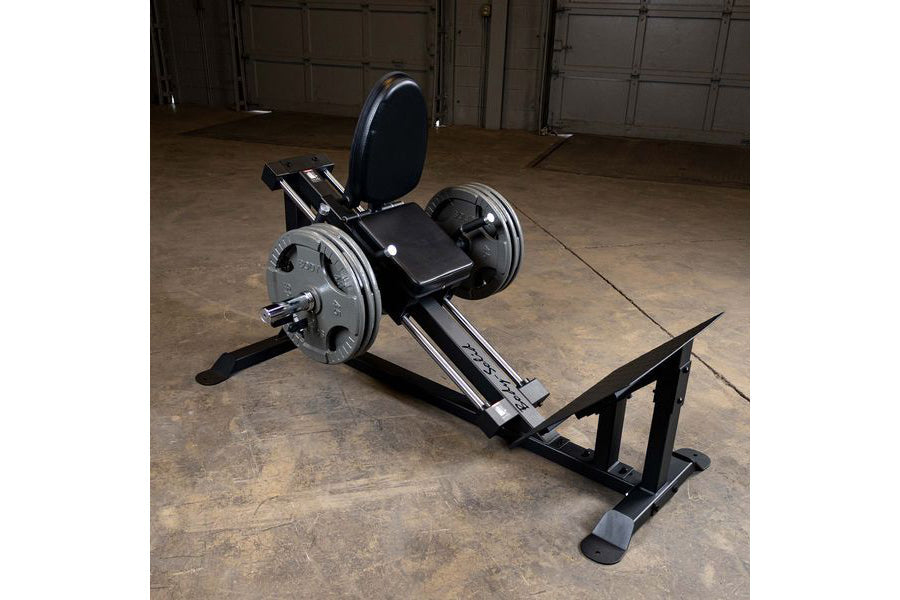 Black and silver leg press machine with padded seat back, weight plate pegs, and footplate on concrete garage floor