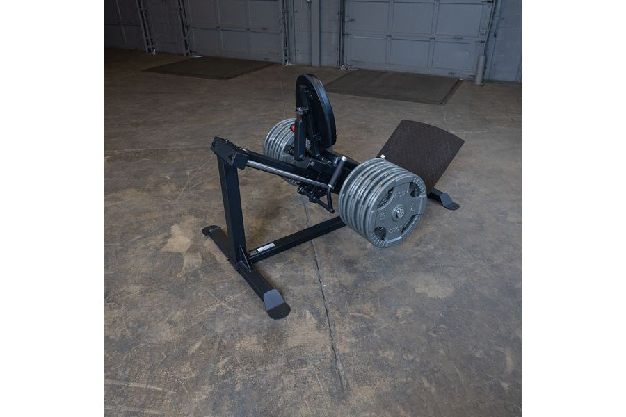 Black compact leg press and hack squat machine with chrome weight plates on concrete garage floor