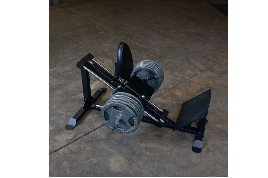 Body-Solid compact leg press and hack squat machine with black frame, dual weight plates, and gray foot platform on concrete 