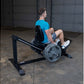 Man wearing blue t-shirt using black Body-Solid leg press machine with weighted barbell in garage gym setting