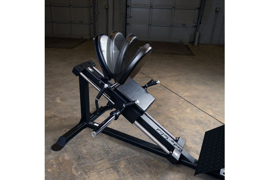 Black and silver compact leg press and hack squat machine with five weight plates loaded on top, displayed in garage setting