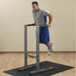 Man using gray dip station with black base mat, wearing gray t-shirt and blue shorts on wooden floor