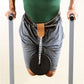 Man wearing green tank top and gray shorts using dip station with black weight plate attached, holding parallel bars on white