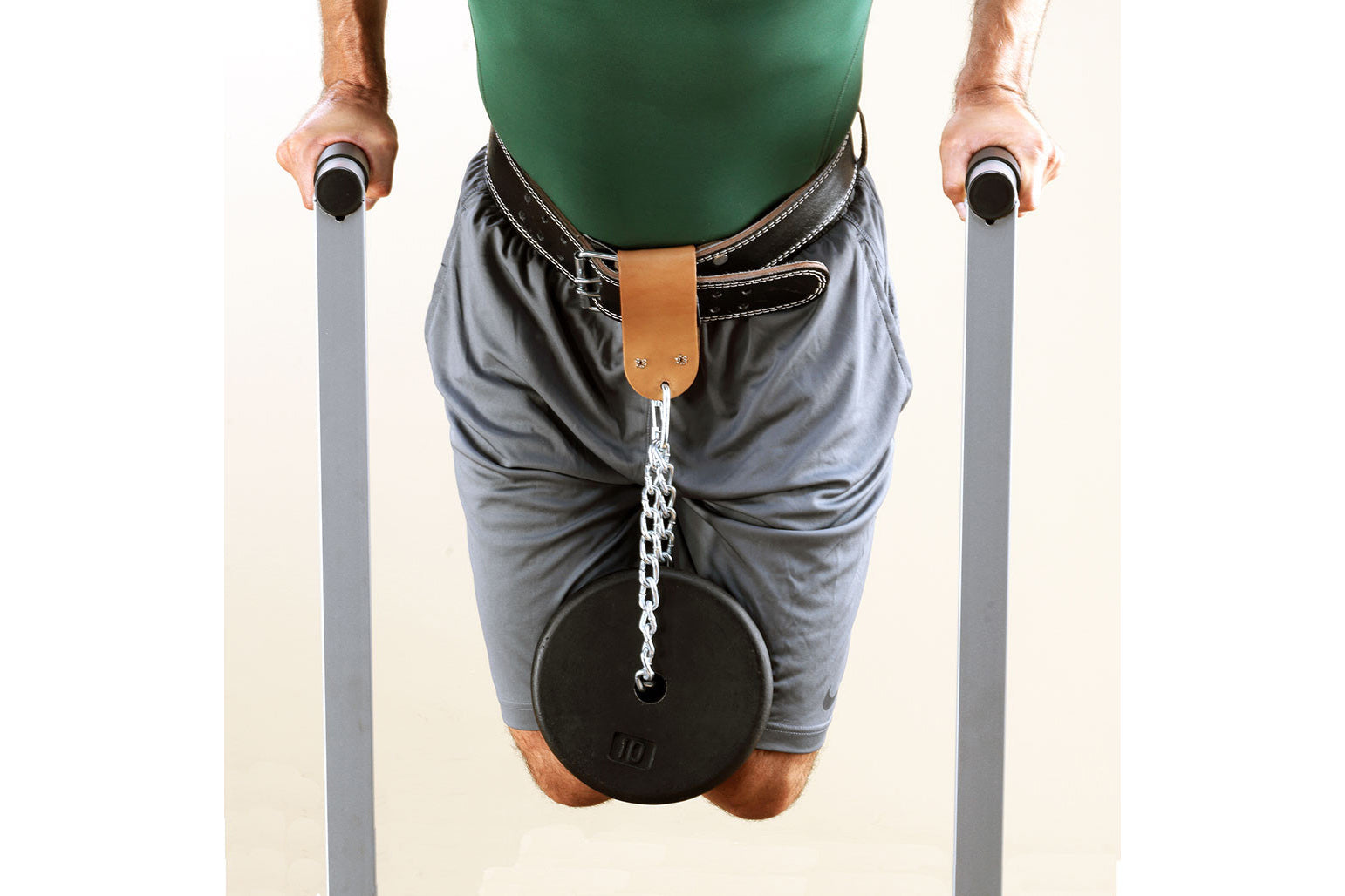 Man wearing green tank top and gray shorts using dip station with black weight plate attached, holding parallel bars on white