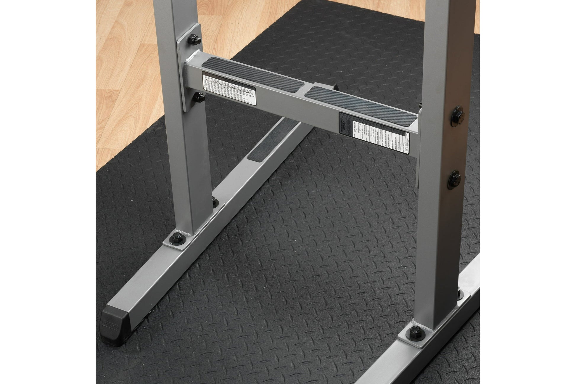 Gray and black dip station with textured diamond plate platform, metal frame, and grip handles on black mat floor