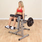 Woman in red sports bra and black shorts using gray and black leg extension machine with weight plate in gym setting