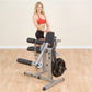 Woman in red sports bra and black shorts seated on Body-Solid leg extension and curl machine with weight plate, shown in gym 