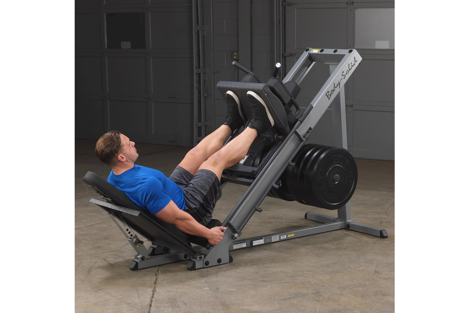 Body-Solid leg press and hack squat machine in gray and black with weighted footplate, shown in use by model in gym
