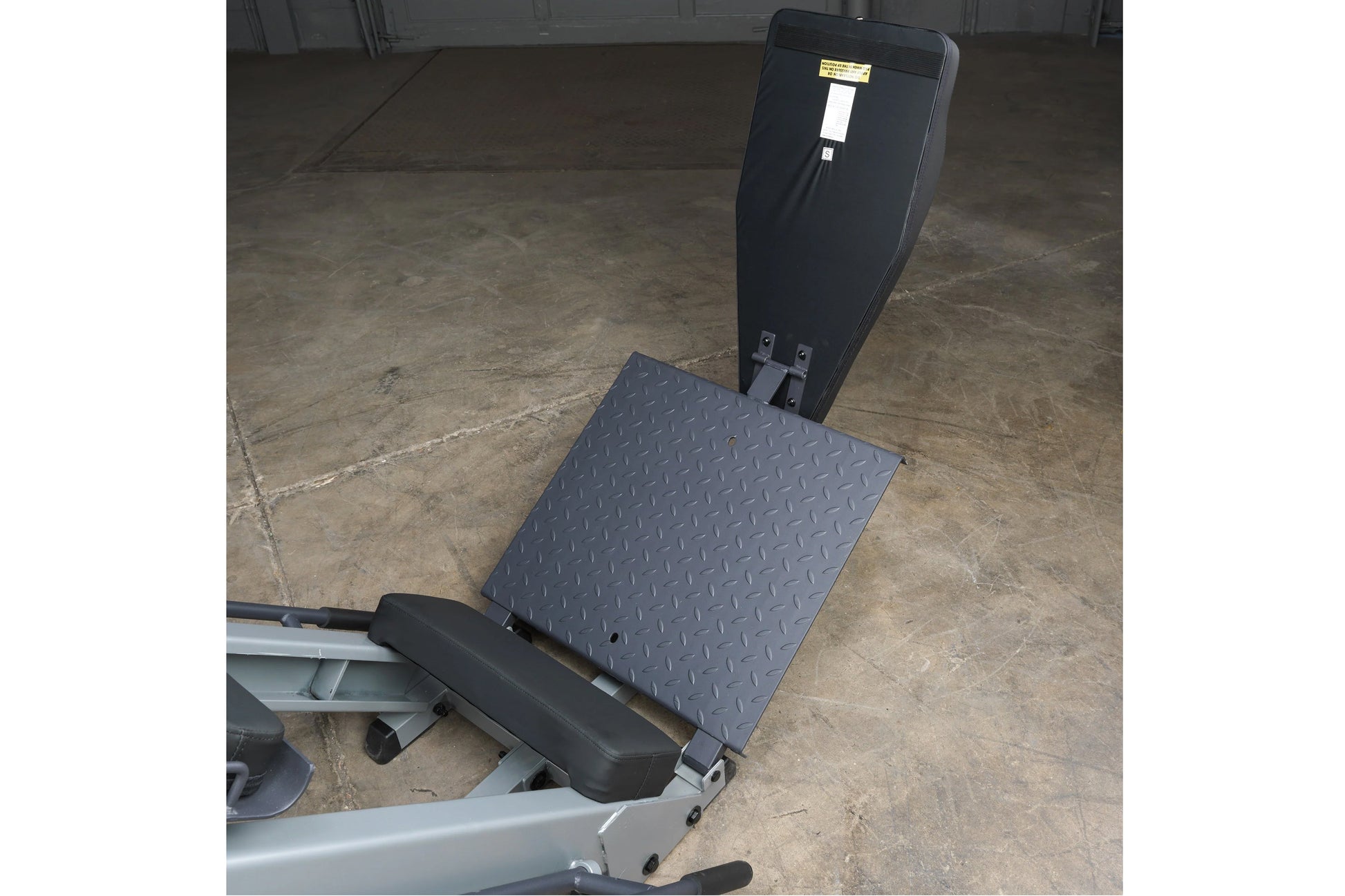 Body-Solid black and gray leg press hack squat machine with diamond plate platform and adjustable backrest on concrete floor