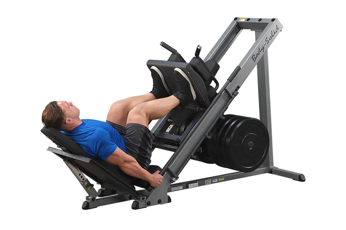 Man in blue shirt using gray and black leg press machine with loaded weight plate, demonstrated on white background