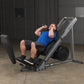 Man in blue shirt using gray and black leg press machine in gym setting
