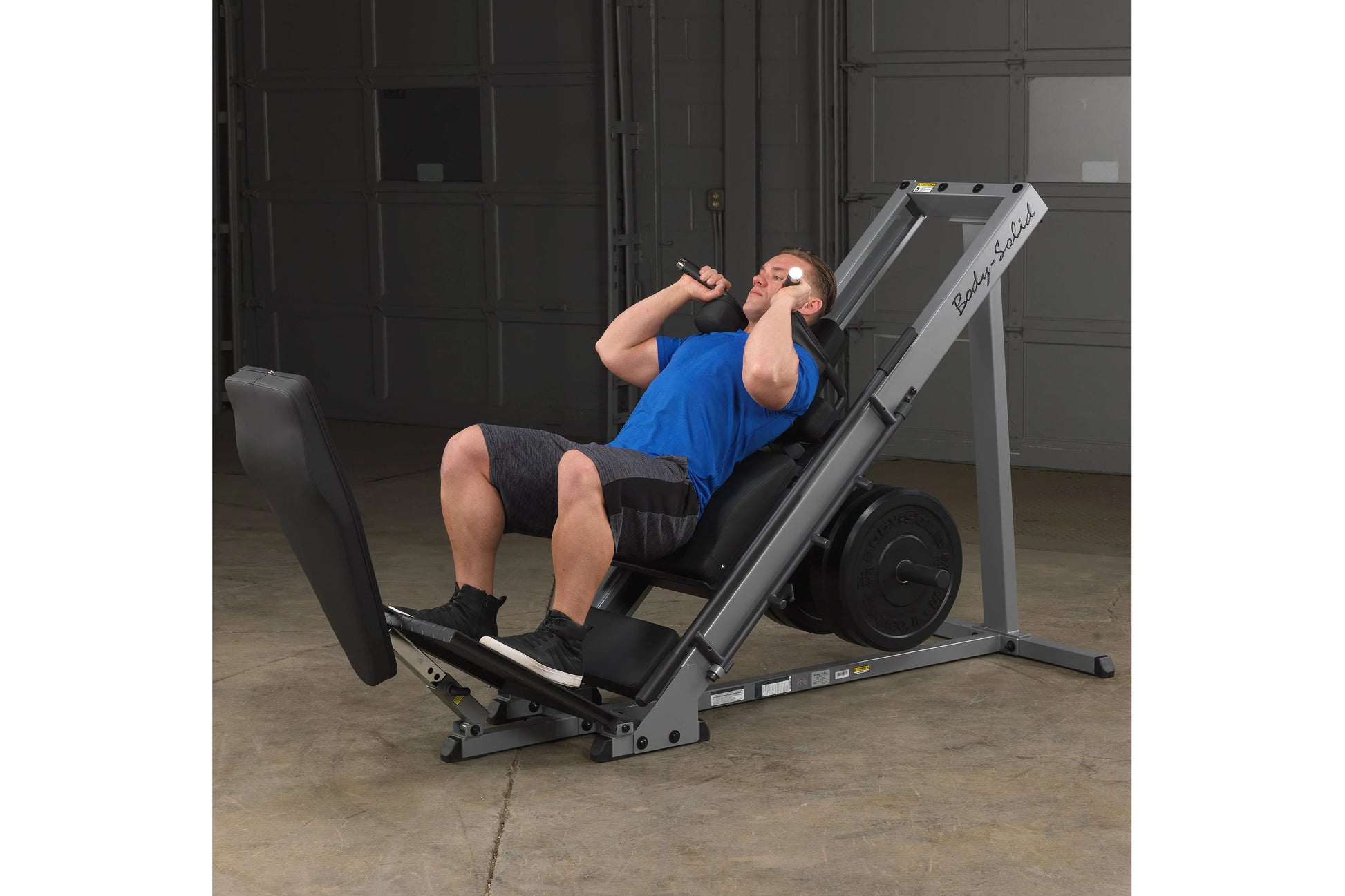 Man in blue shirt using gray and black leg press machine in gym setting