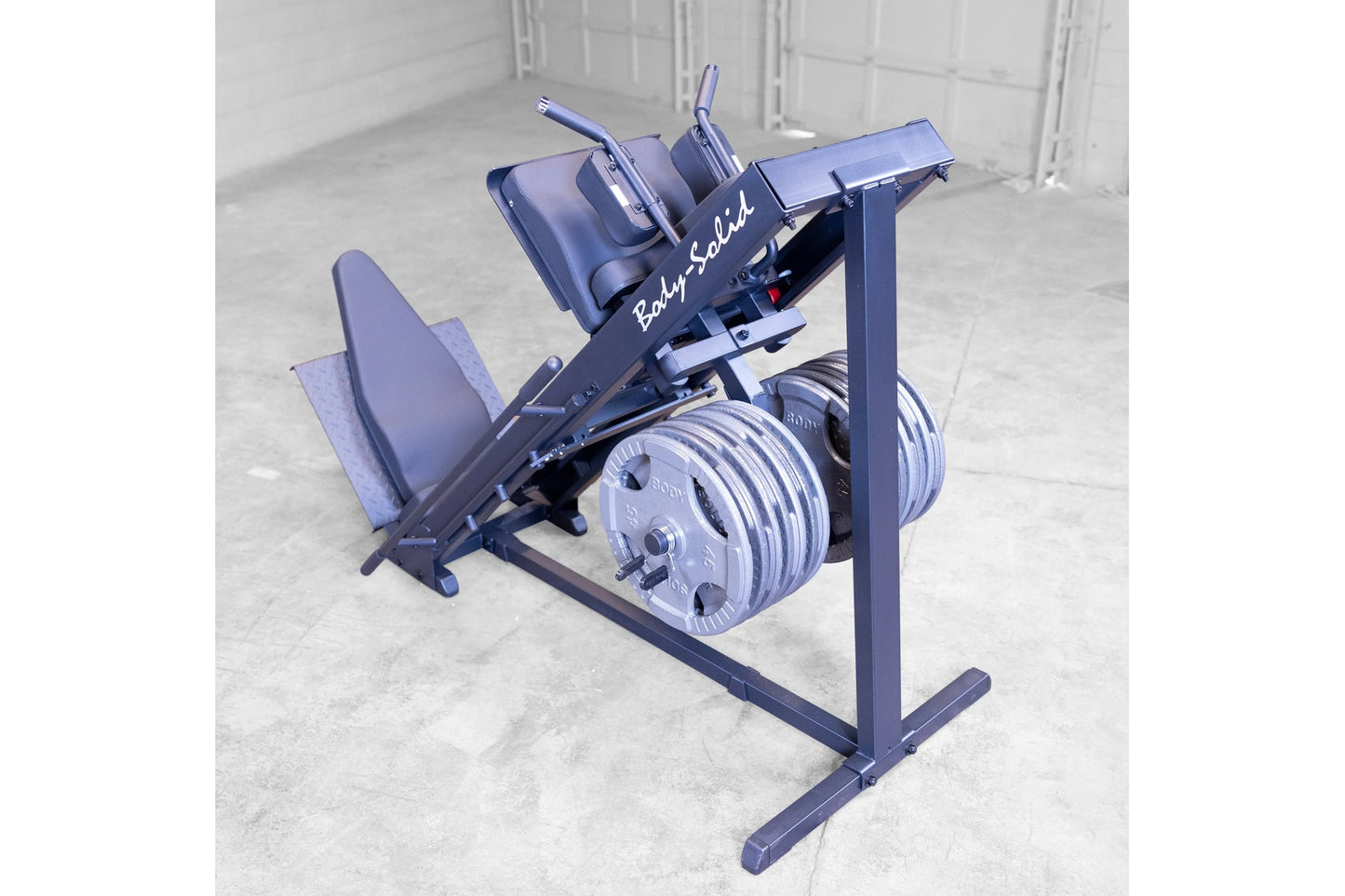 Body-Solid leg press and hack squat machine in navy blue with padded seat, dual weight plate pegs, and adjustment handles on 