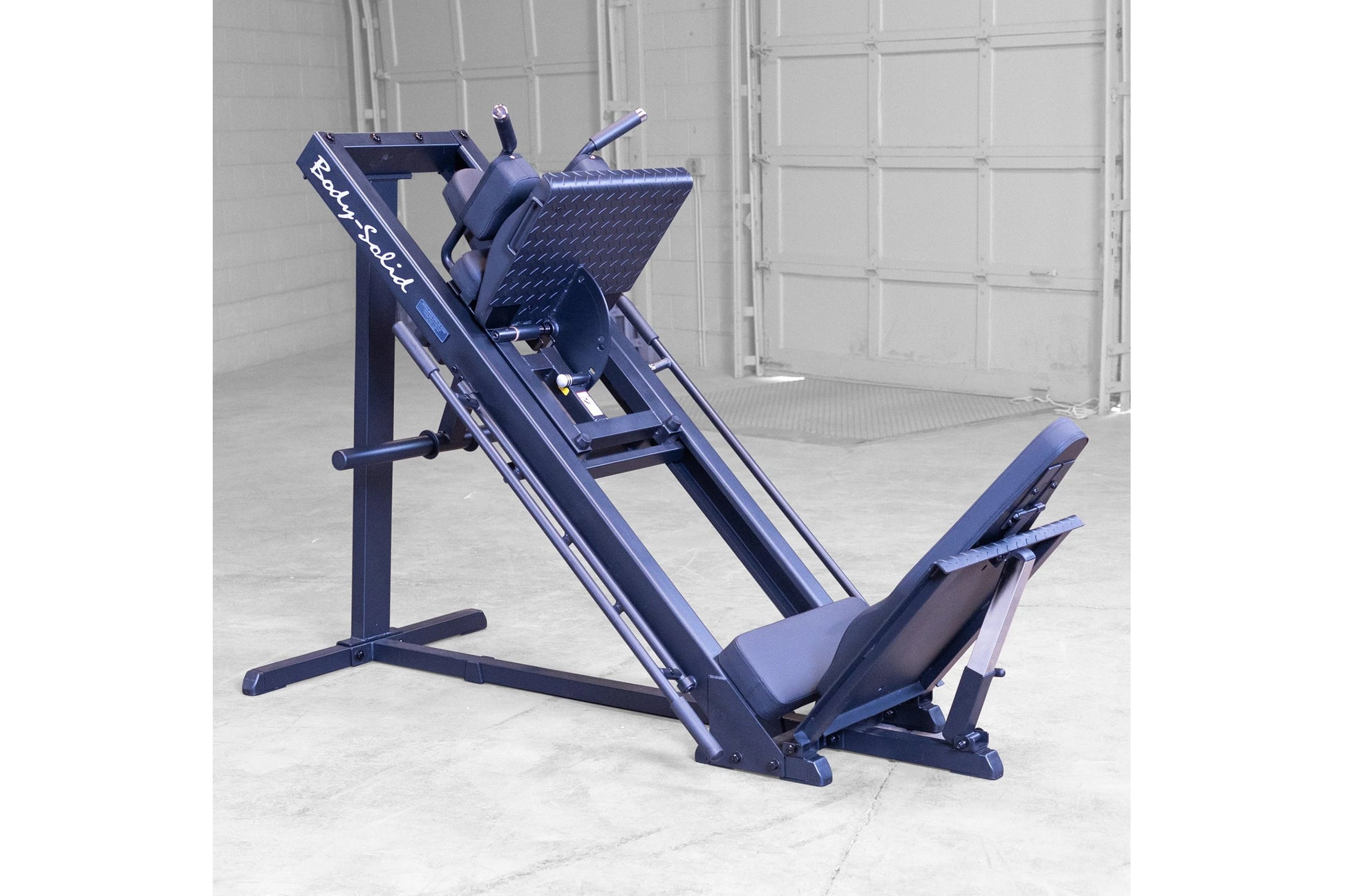 Navy blue leg press and hack squat machine with padded seat and foot platform, displayed in garage setting