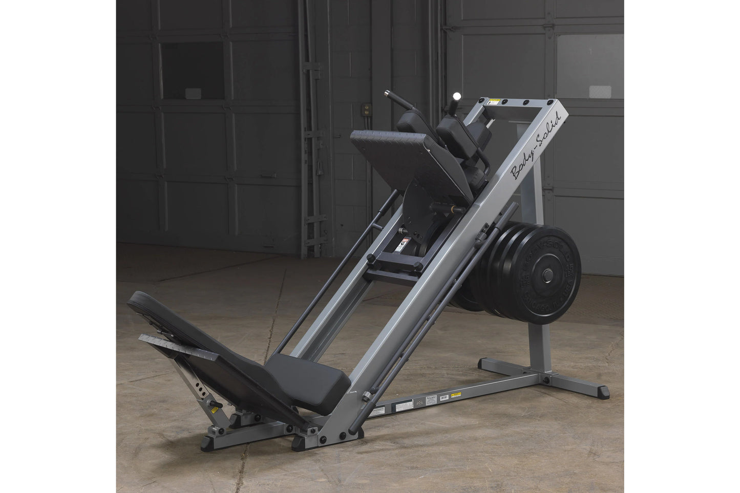 Body-Solid leg press and hack squat machine with silver frame, black seat and footplate, loaded with black weight plates, in 
