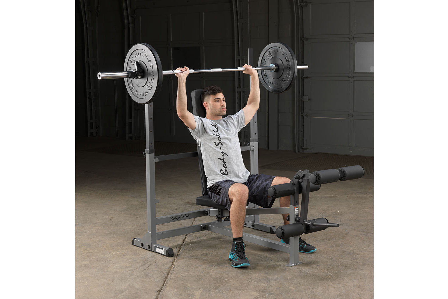 Man using gray and black weight bench with barbell and black weight plates in gym setting