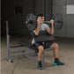 Man performing barbell shoulder press on black Body-Solid weight bench with loaded barbell in industrial gym setting