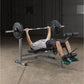 Man performing bench press with loaded barbell on gray weight bench in gym setting