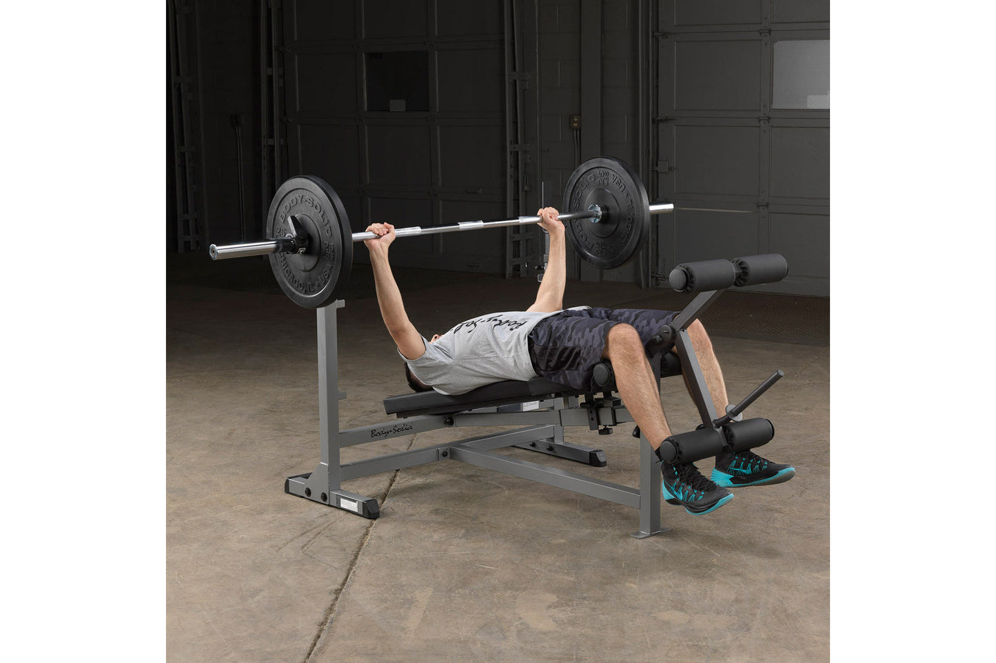 Man performing bench press with loaded barbell on gray weight bench in gym setting