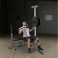 Man performing shoulder press on silver and black weight bench with loaded barbell in gym setting