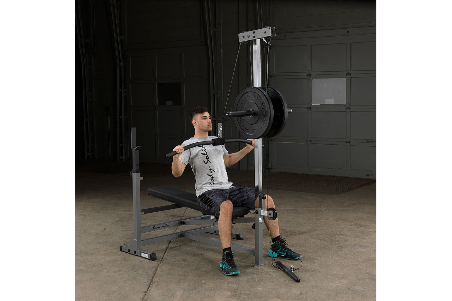 Man performing shoulder press on silver and black weight bench with loaded barbell in gym setting