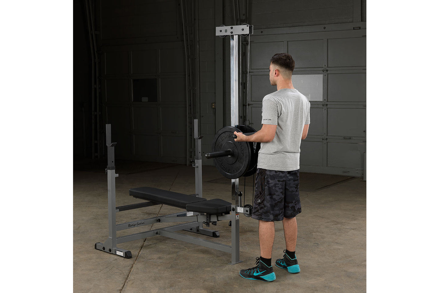 Body-Solid PowerCenter Combo Bench with barbell attachment, gray steel frame and black seat, worn by male model in garage gym