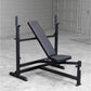Black weight bench with incline backrest, leg extension attachment, and adjustable barbell uprights on concrete floor