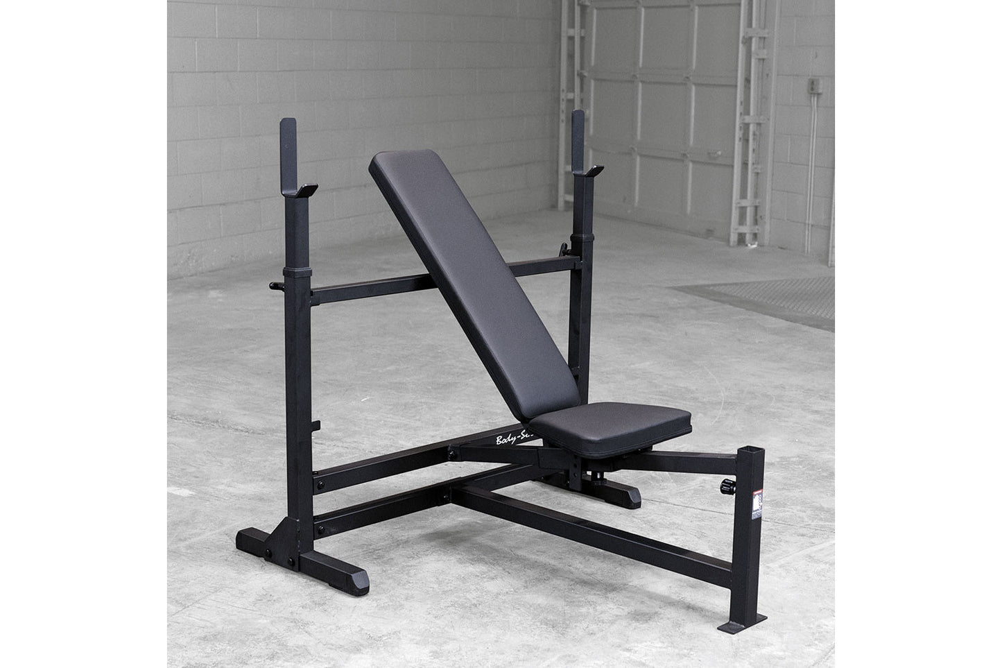 Black weight bench with incline backrest, leg extension attachment, and adjustable barbell uprights on concrete floor