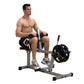 Man using silver and black seated calf raise machine with weighted barbell, demonstrating exercise form on white background