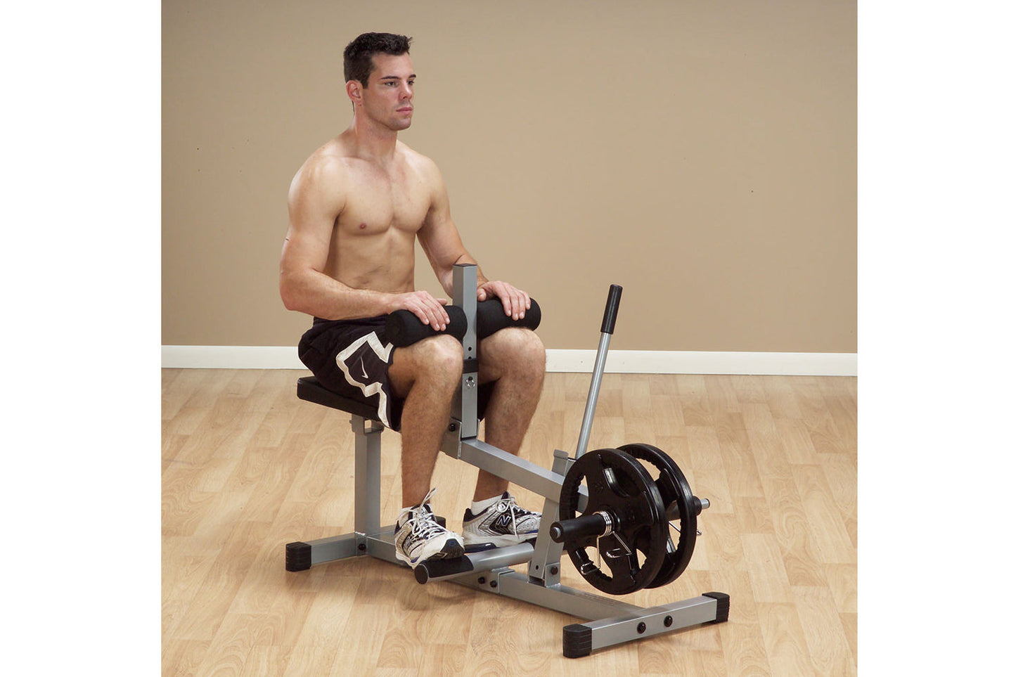 Man demonstrating Body-Solid PowerLine Seated Calf Raise Machine with gray frame and black weight plate on wooden floor