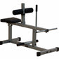 Seated calf raise machine with gray steel frame, black padded seat, cylindrical leg rest, and foot platform on white backgrou