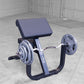 Black and blue preacher curl bench with curved pad and barbell arms, loaded with weight plates on concrete floor